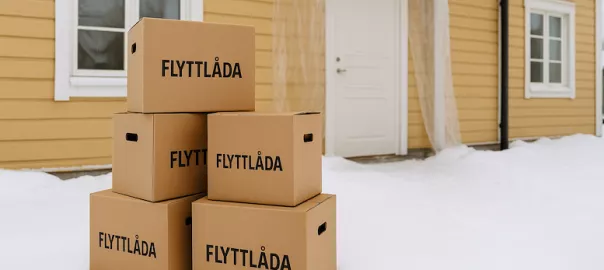 “Flyttlådor står i snön utanför hus under vinterflytt – symboliserar flytt i kallt klimat med utmaningar som kyla och snö”